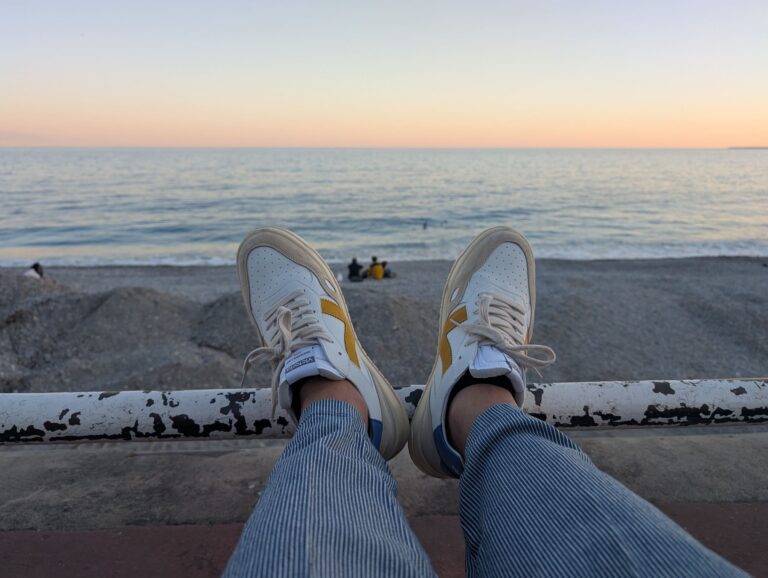 Person relaxing by the seaside at sunset, wearing casual sneakers and striped pants, overlooking calm ocean waves