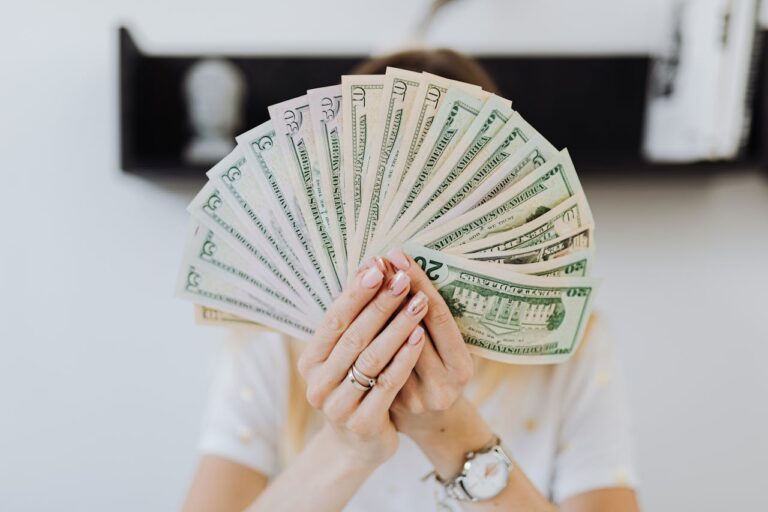 Person holding a fan of cash in front of their face, representing quiet wealth and personal finance.