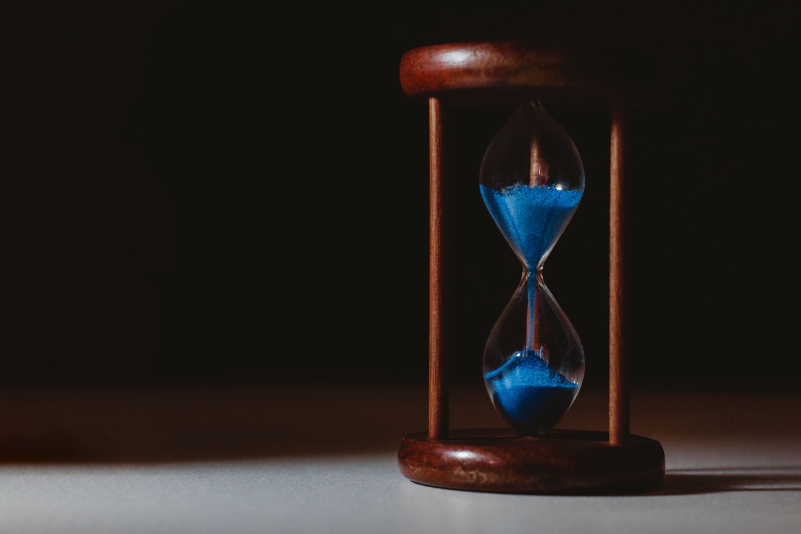Wooden hourglass with blue sand on a dark background, representing a fixed, automated investing schedule