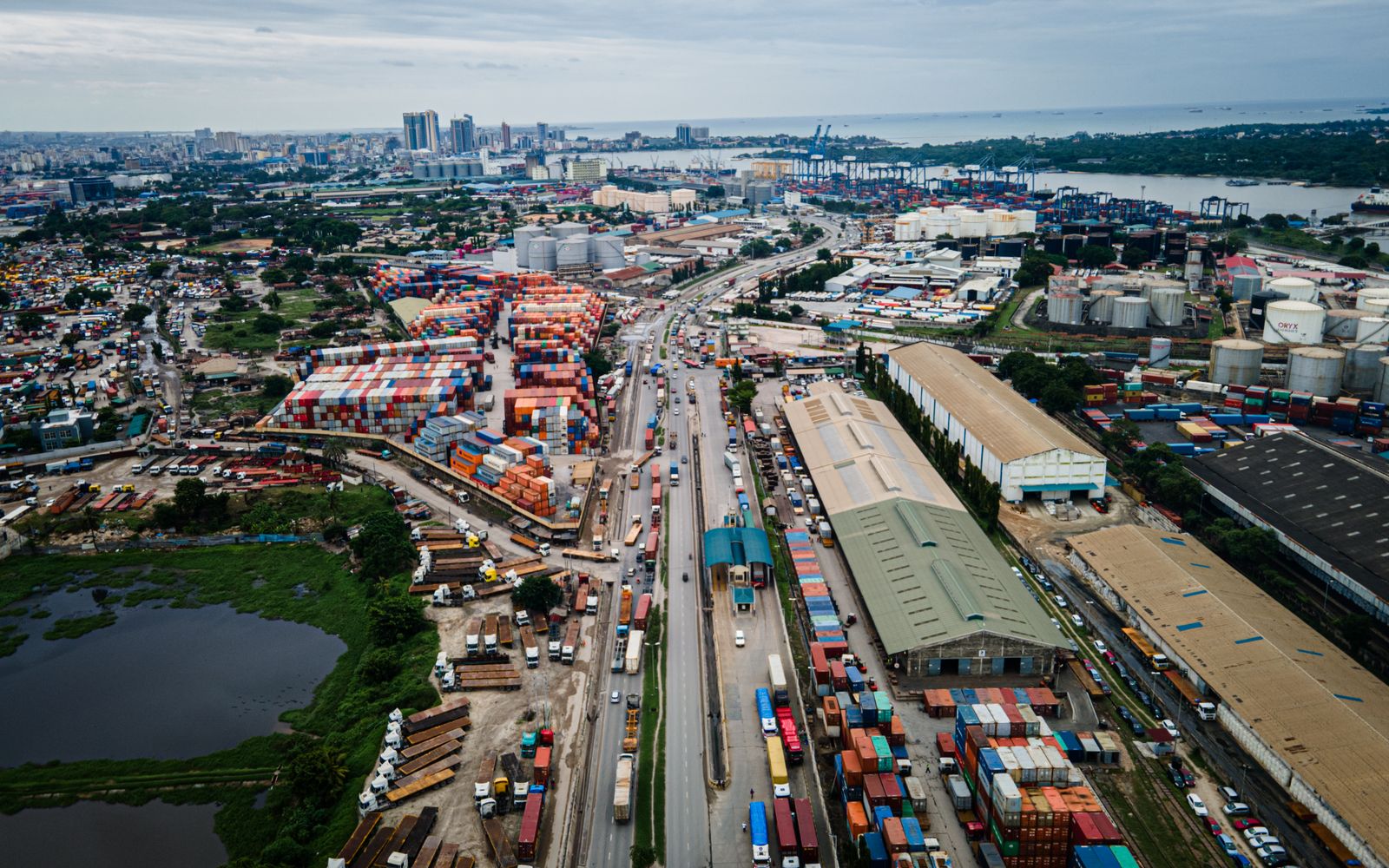Aerial view of a city port with container yards, warehouses, fuel storage tanks and a distant skyline, like distinct sectors of the economy
