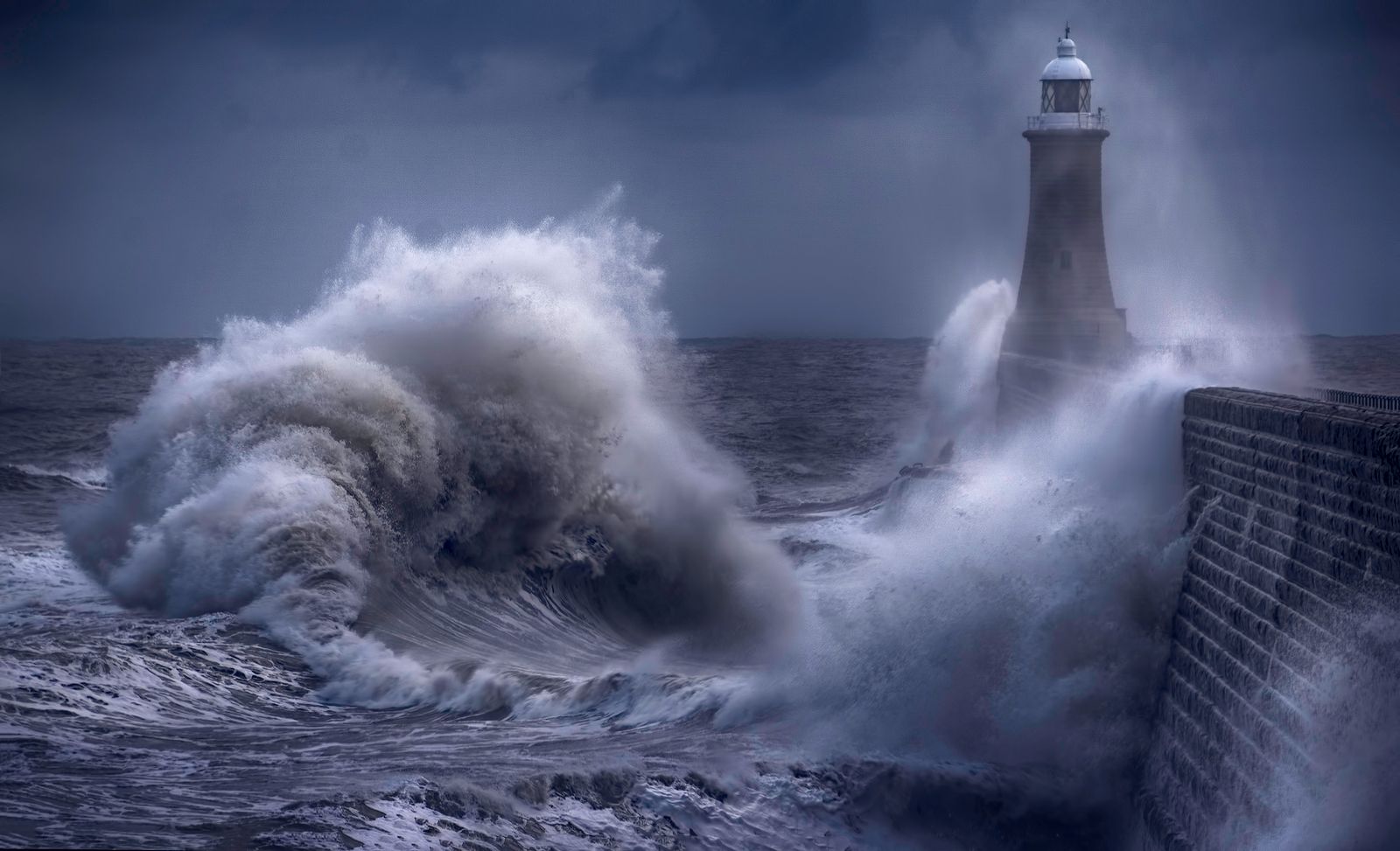 Lighthouse on a stone pier battered by large storm waves, symbolizing defensive sectors during market downturns